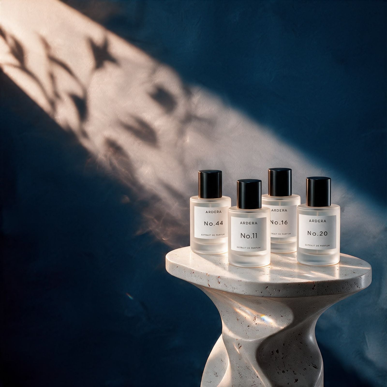 Four ARDERA Extrait de Parfum bottles, No.44, No.11, No.16 and No.20, on a travertine pedestal in soft afternoon light